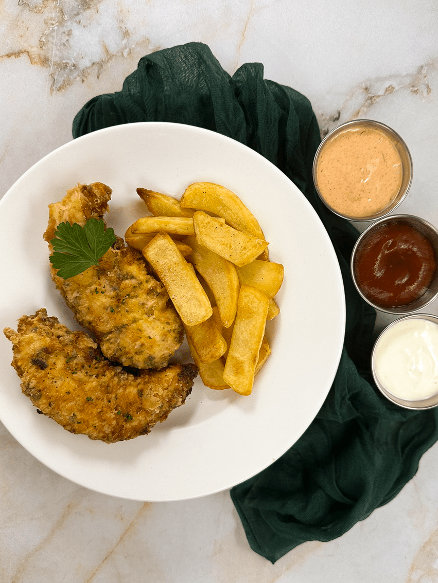 A round white plate topped with two fried Cajun chicken tenders and fries alongside a green napkin and three dipping sauces.