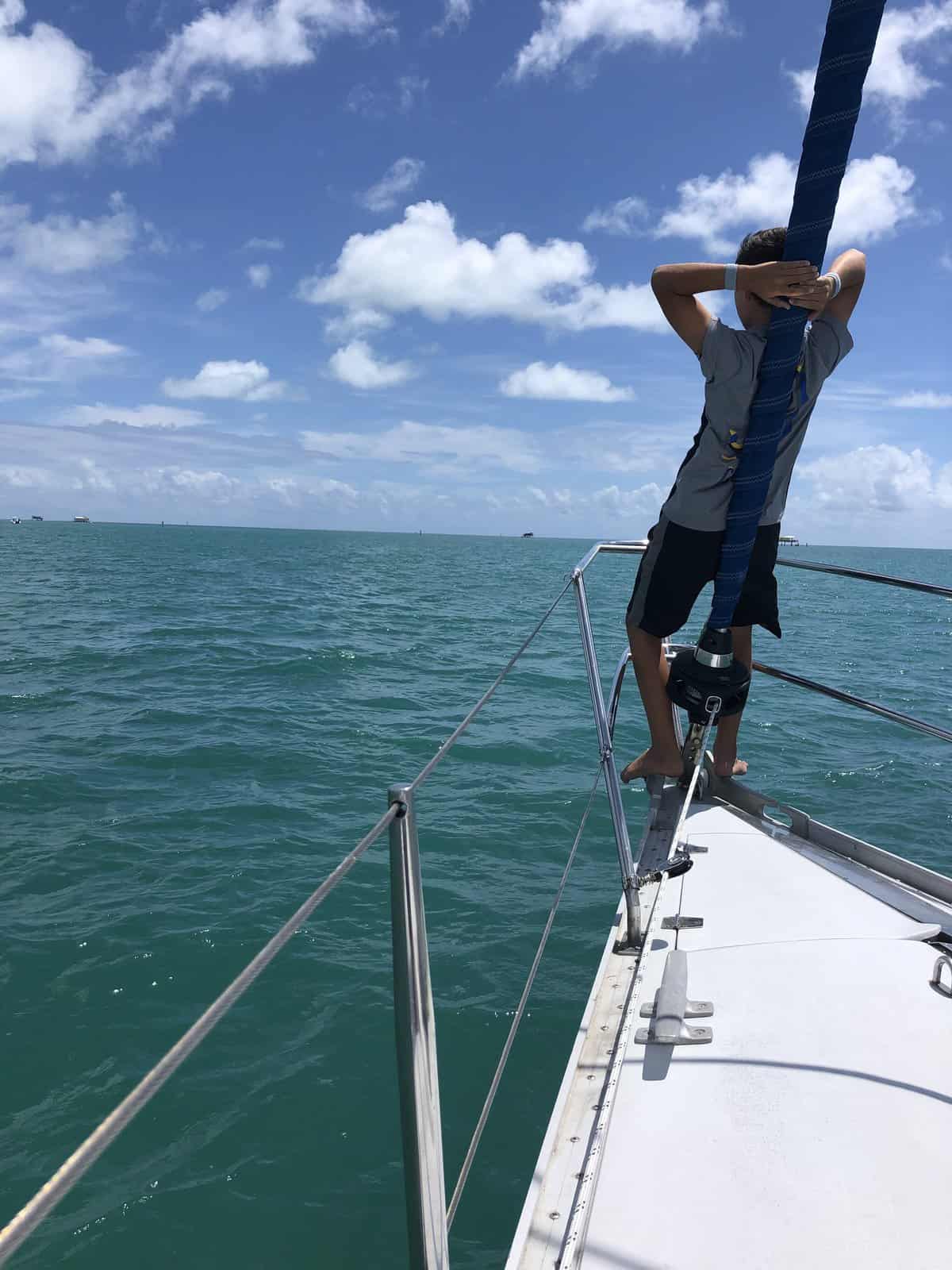 A boy on the bow of a sailboat, with the sea horizon in front