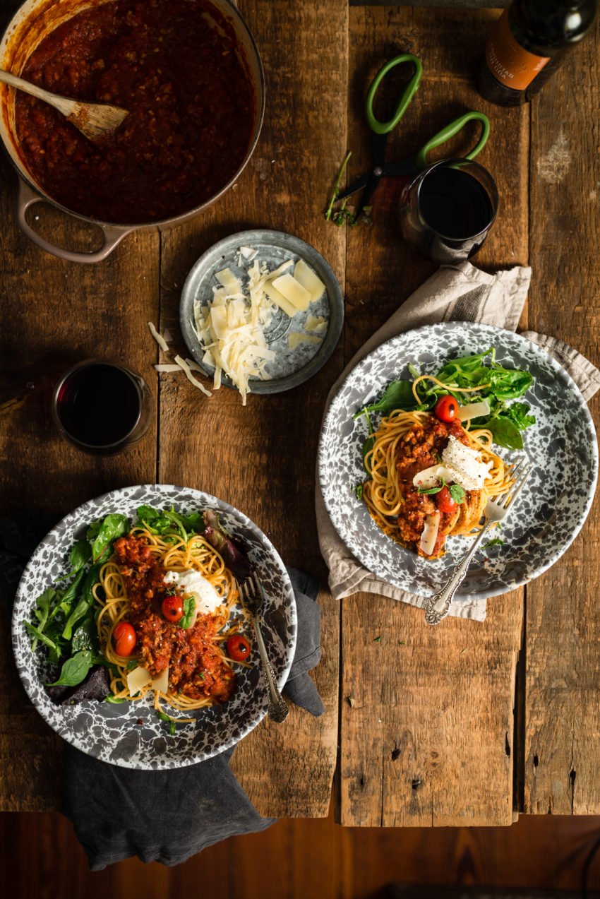 an above shot of two dishes with pasta and sacuce on top sprinkled with parm and greens on the side.
