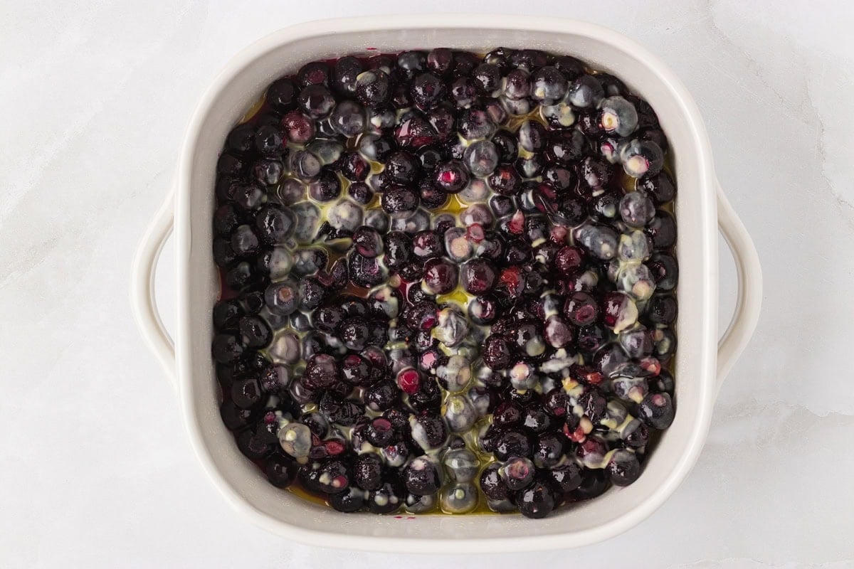 Blueberry filling poured into a white baking dish and topped with melted butter.
