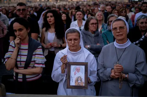 NurPhoto via Getty Images A nun holds a picture of Pope Francis as the faithful gather for Rosary prayers in honour of Pope Francis at St. Peter's Square