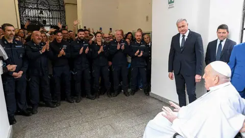 Vatican Media Pope Francis sits in a wheelchair as prison staff applaud him
