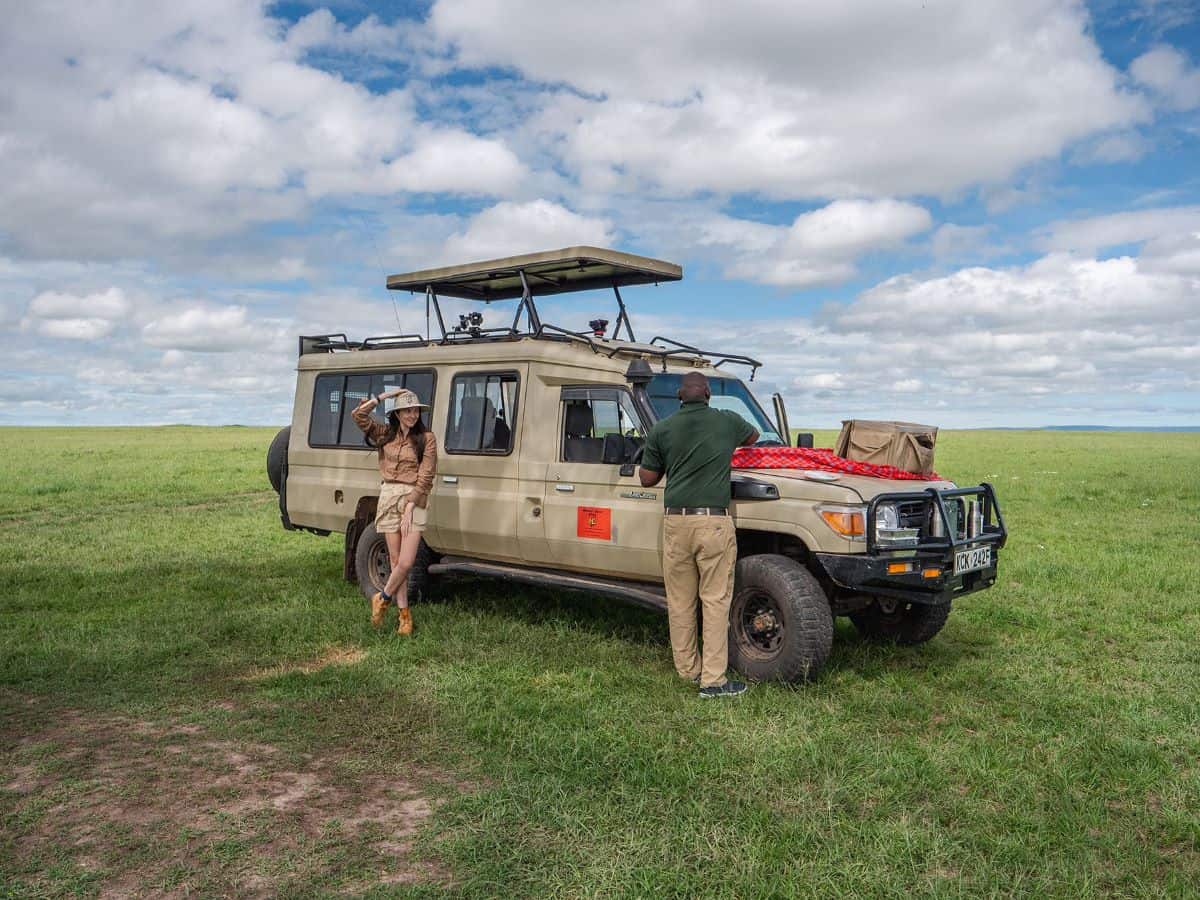 a solo female traveler on safari in Tanzania leaning against a safari vehicle in front of a view of endless plains
