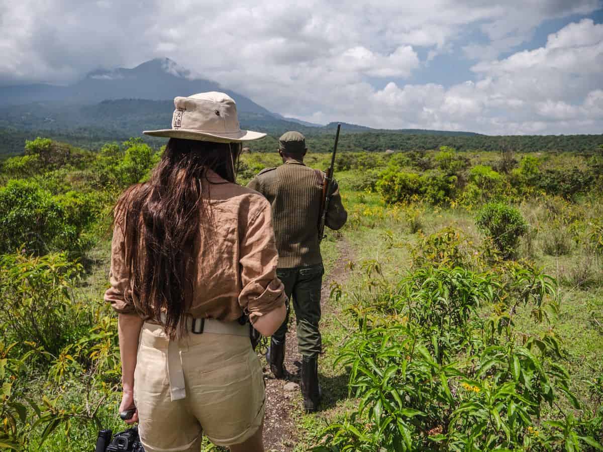 A solo female traveler walking behind a guide during a walking safari in Arusha National Park, Tanzania, with Mount Meru in the background.