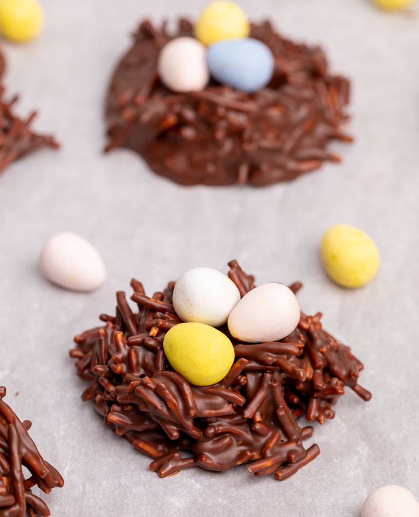 side image of brown chocolate no bake cookie with thin chow mein noodles mixed in and topped with 3 mini egg shaped candies with yellow, pink and white coatings