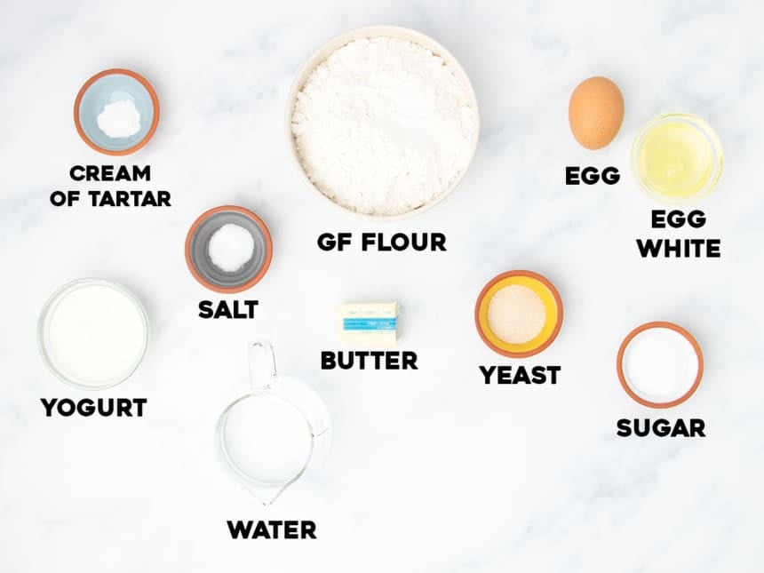 ingredients for making gluten free naan bread in small bowls on light marble surface with black block letters spelling names of ingredients