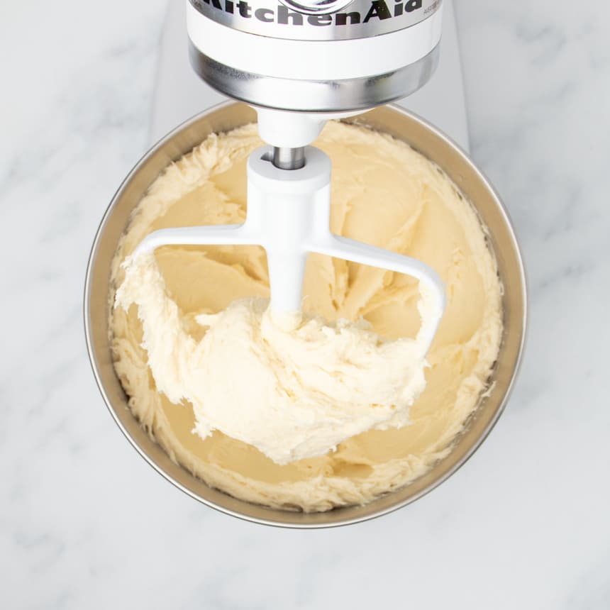 white stand mixer paddle attachment with very soft pale batter on paddle and in bowl below it