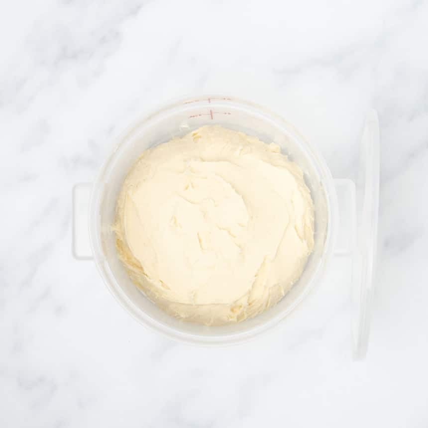 pale dough in clear round proofing bucket with cover on its side leaning against bucket