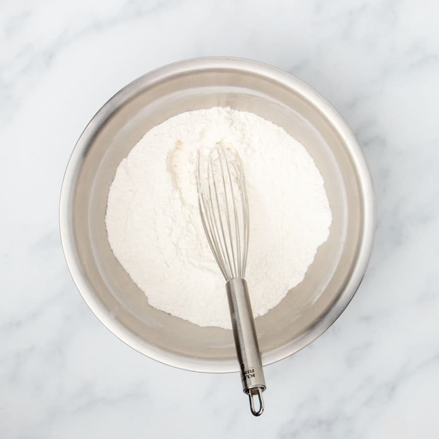 large round metal mixing bowl with white flour mixture and large metal wire whisk