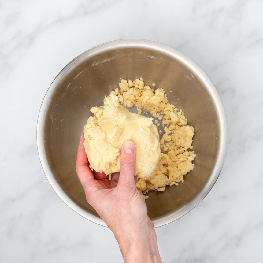 hand holding very pale yellow raw sugar cookie dough pressed into a large clump