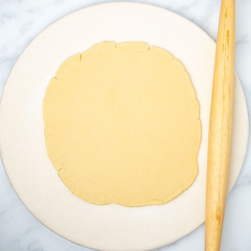 same raw dough rolled into 1/3-inch round with blond wood French rolling pin