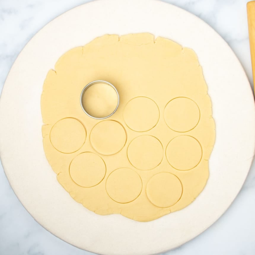raw round of rolled out dough with 9 rounds cut and round metal cookie cutter sitting on dough