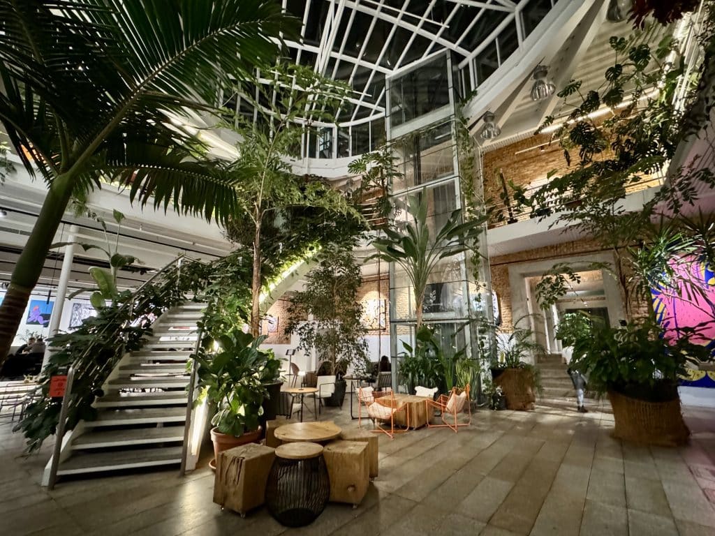 A restaurant interior with tons of plants everywhere, including curling up a curved staircase.