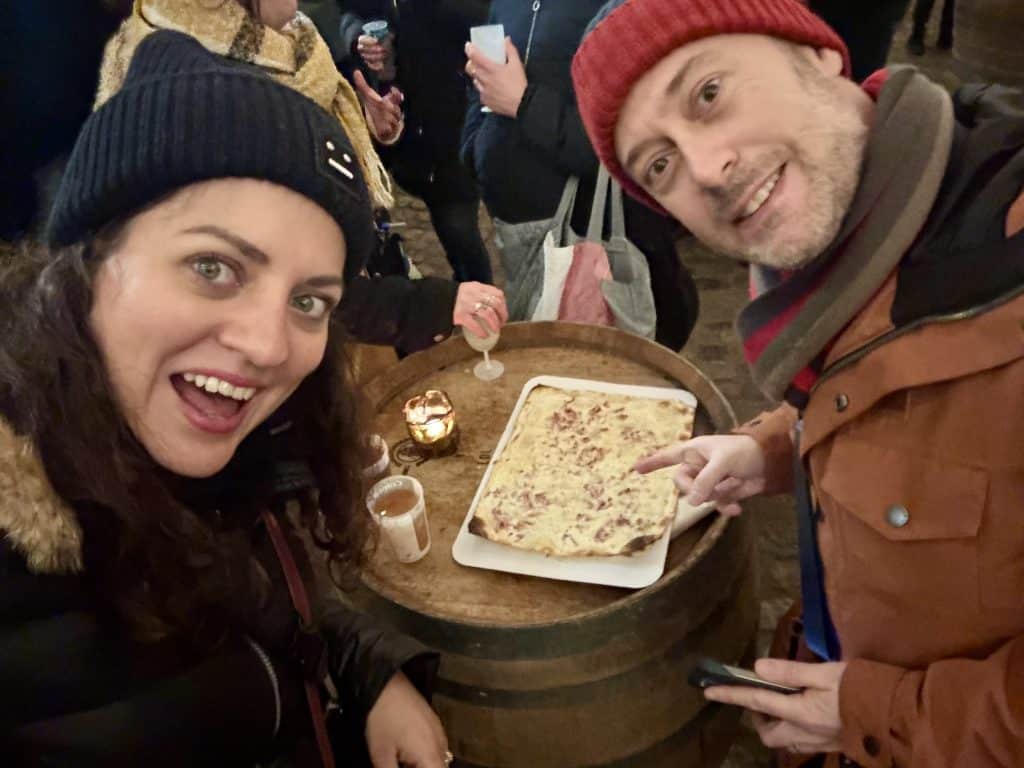 Kate and Charlie taking a selfie with a tarte flambée on the table between them.