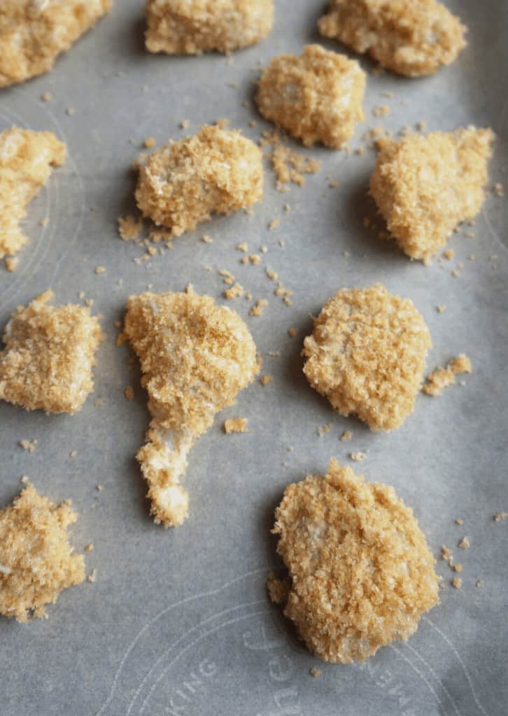 The breaded chicken on a baking sheet ready to be cooked.