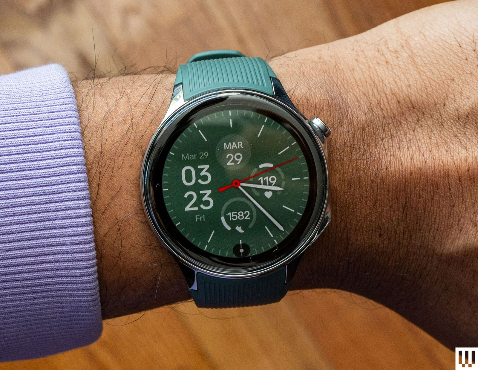 Overhead view of the OnePlus Watch 2 wristwatch with a green band on a wrist.