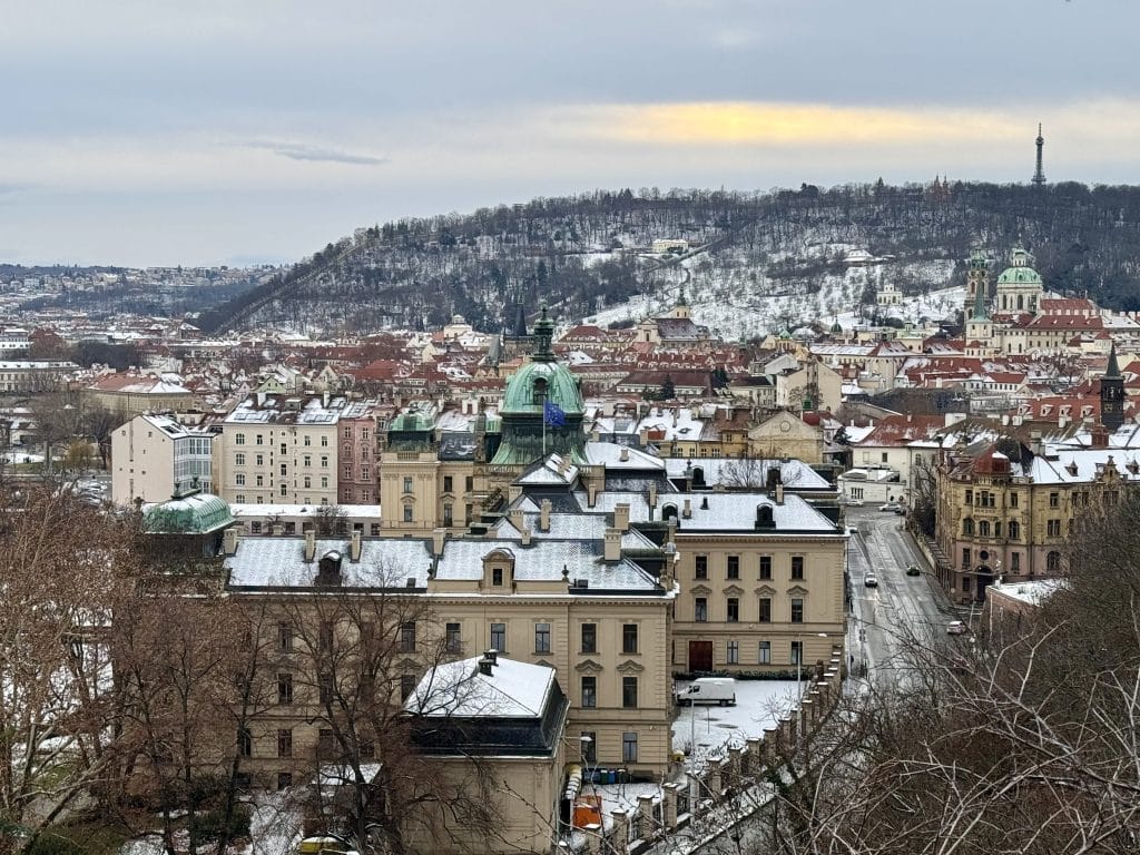 The city of Prague viewed from above, with lots of old-fashioned buildings topped in a dusting of snow.