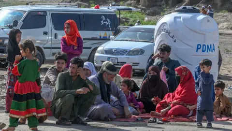 Getty Images A scene at the Torkham crossing showing men, women and children sitting on the floor. There are several vehicles in the background.