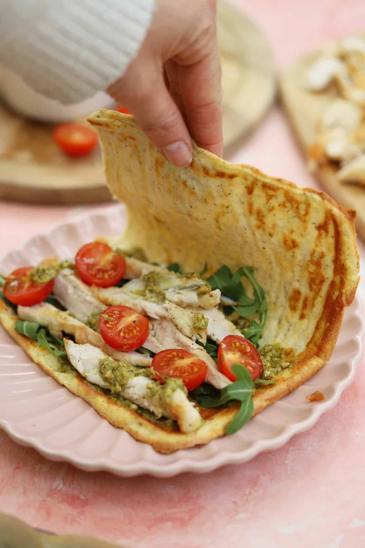 A hand folding a cottage cheese flatbread over a filling of chicken, tomato and rocket.
