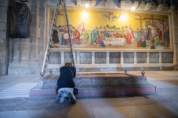 A woman prays kneeling before the Stone of Anointing at the entrance of the Basilica of the Holy Sepulcher in Jerusalem. The stone commemorates the preparation of Jesus’ body with oils and balms before burial. Credit: Marinella Bandini