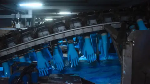 Getty Images A line of blue rubber gloves hanging on a production line in a dimly lit room