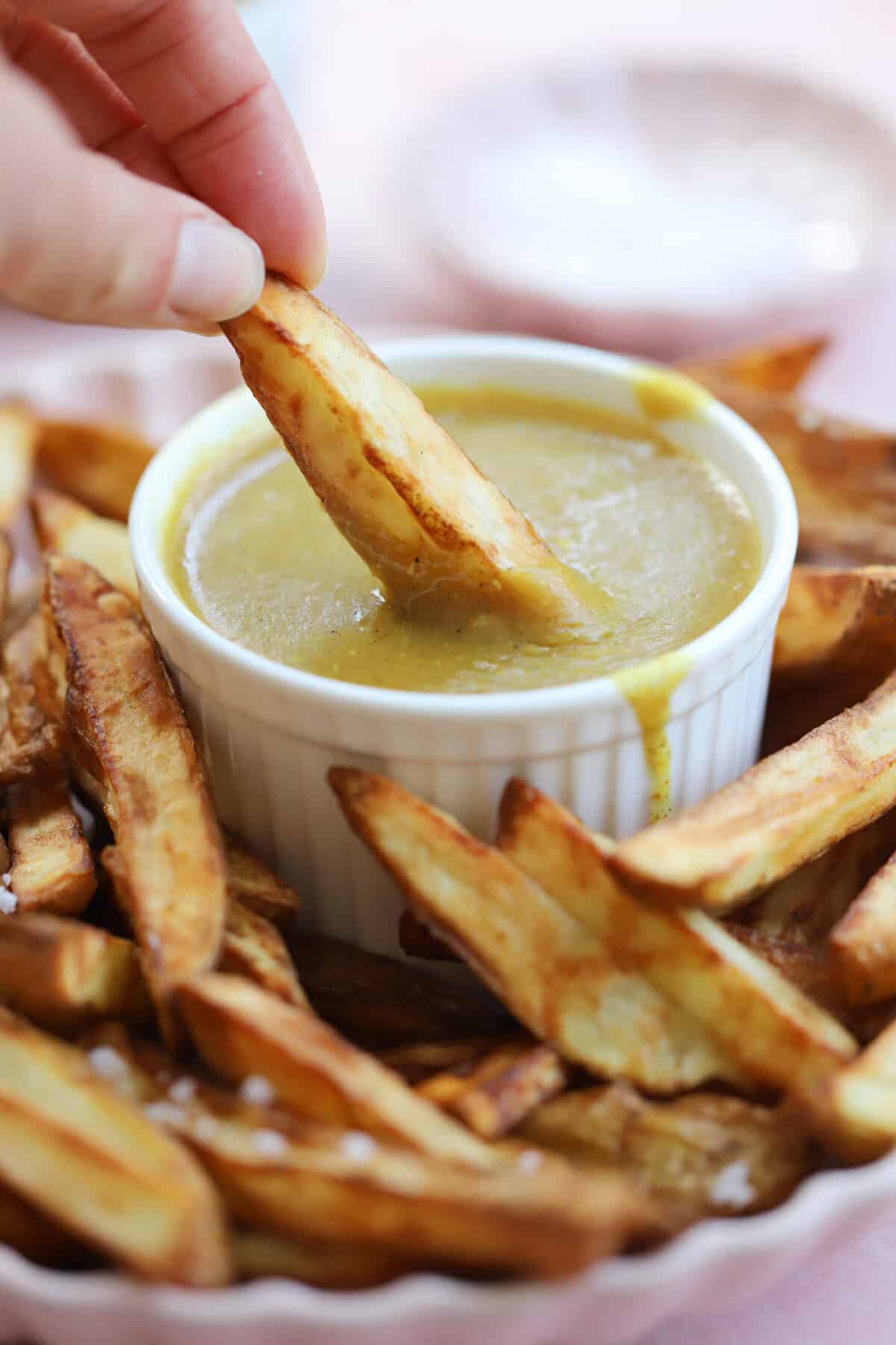 A hand dunking a chip into a small bowl of gluten free curry sauce, surrounded by chips.