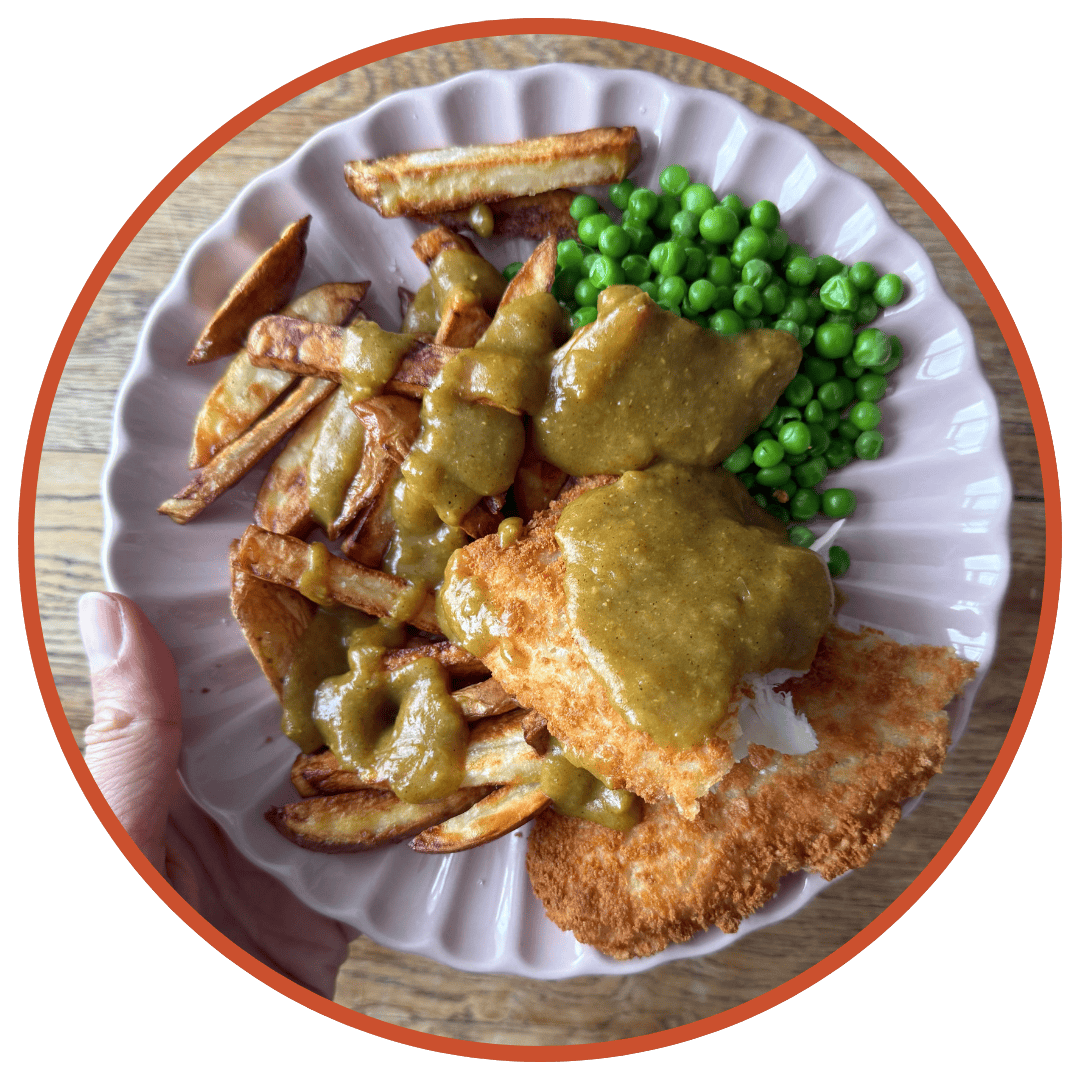 Hand holding a plate of fish and chips with curry sauce.