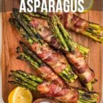 Grilled bacon-wrapped asparagus on a wooden board with lemon slices and salt. Text reads "How to Make Grilled Bacon-Wrapped Asparagus.