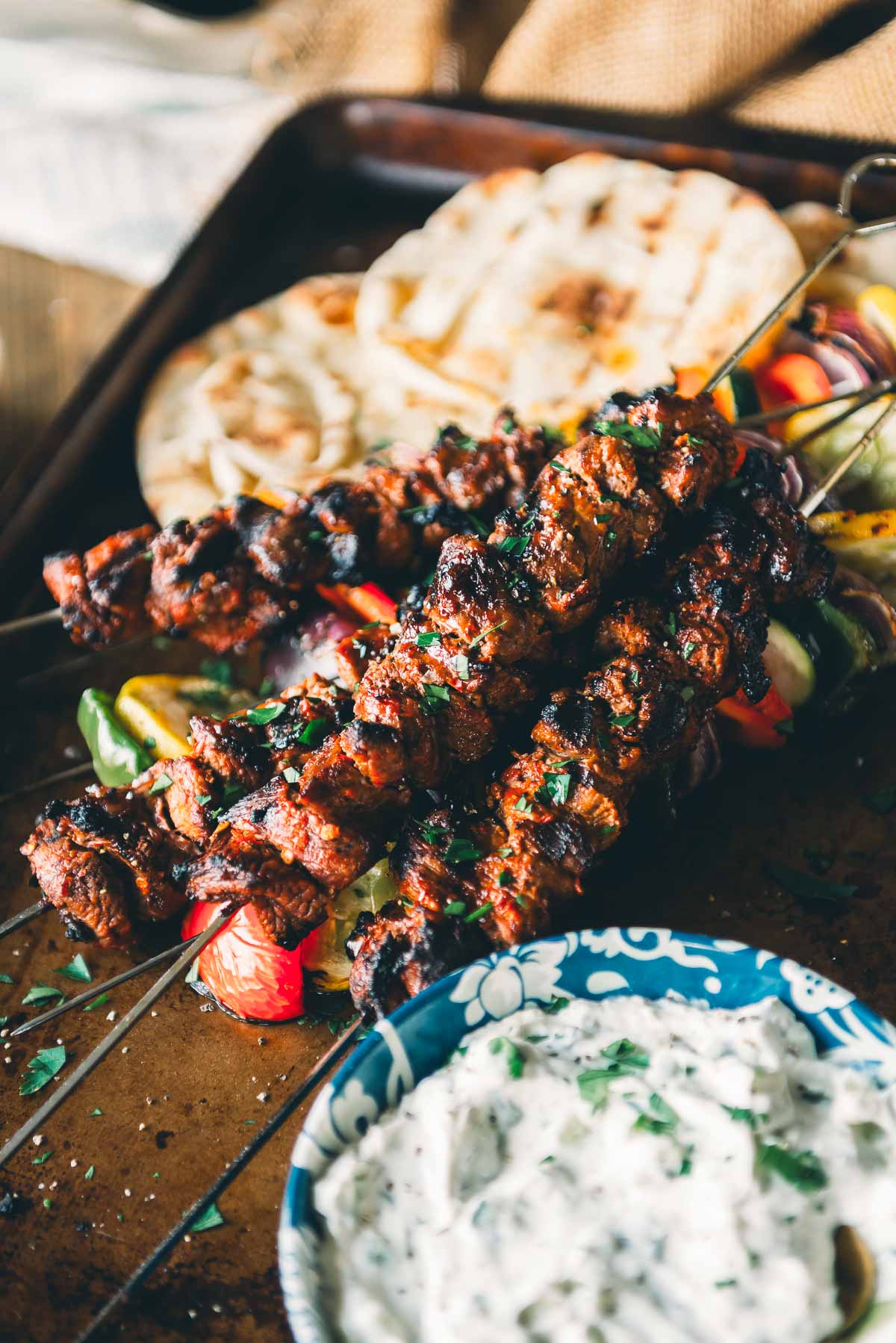 Grilled meat skewers with vegetables are served on a tray with pita bread and a bowl of tzatziki sauce.