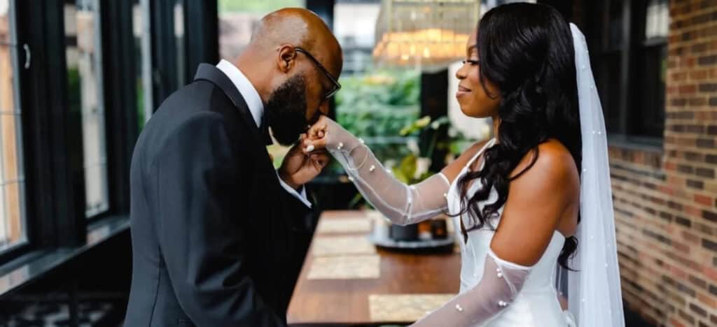 Groom kissing bride's hand in industrial-looking venue