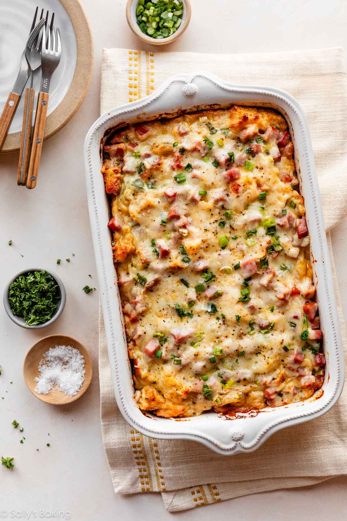ham and Swiss cheese strata in white baking dish with chives, parsley, and sea salt.