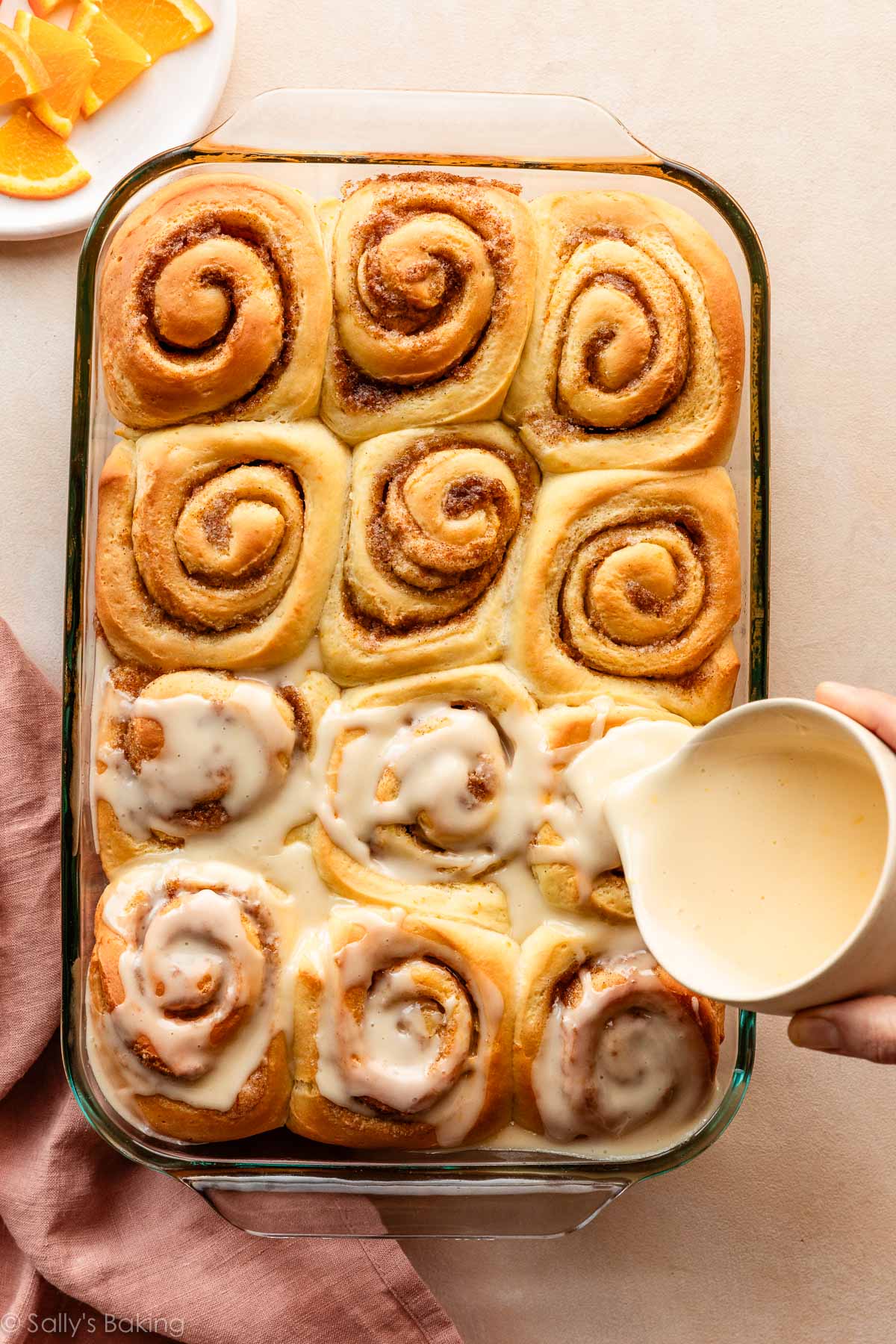pouring orange icing on orange sweet rolls.