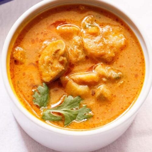 mushroom masala curry garnished with a coriander sprig in a white bowl.