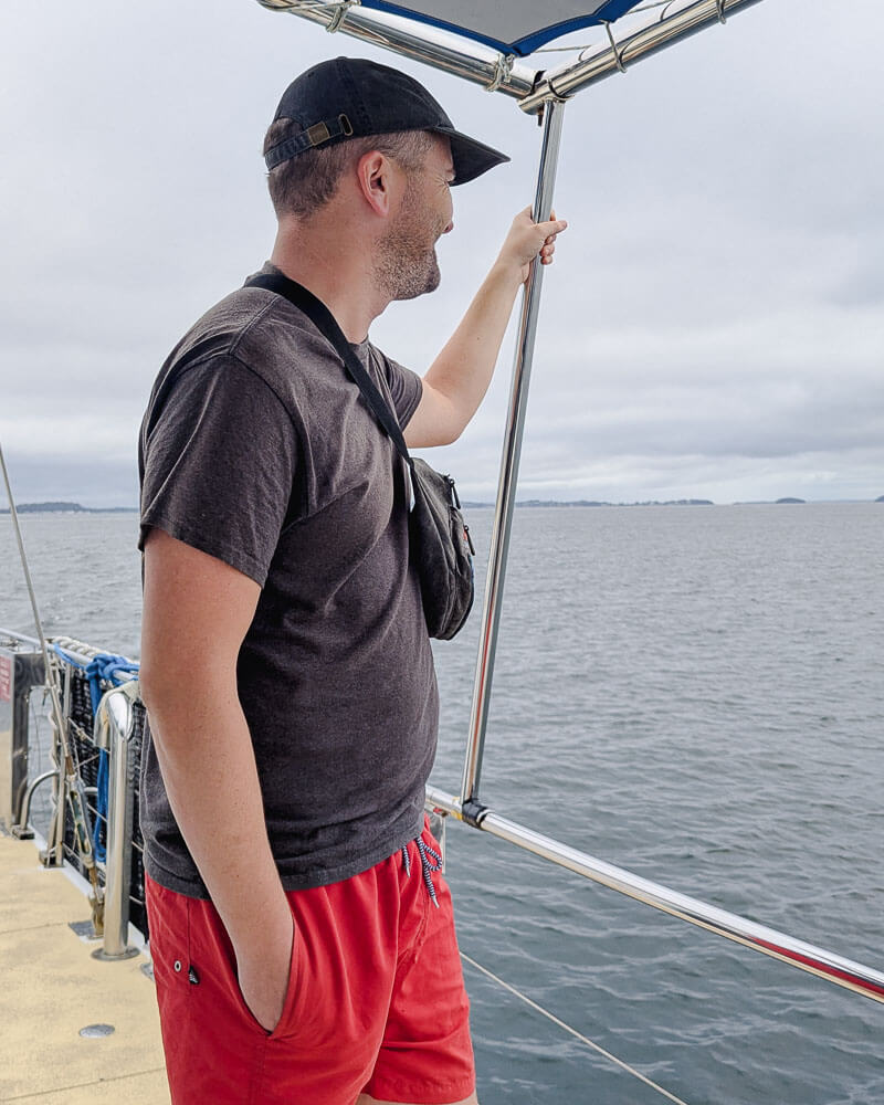 Man standing on deck of a small catamaran looking out onto the water