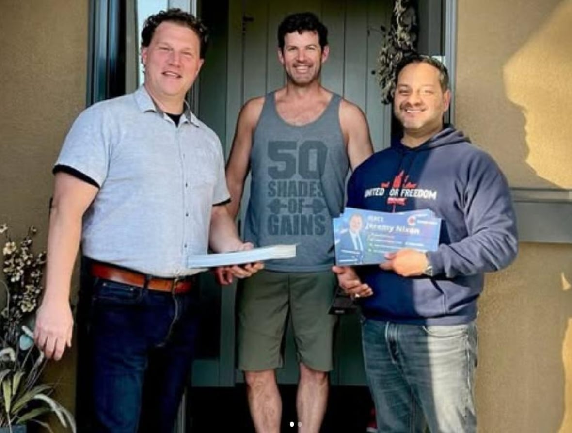 three men standing by a door, two with pamphlets