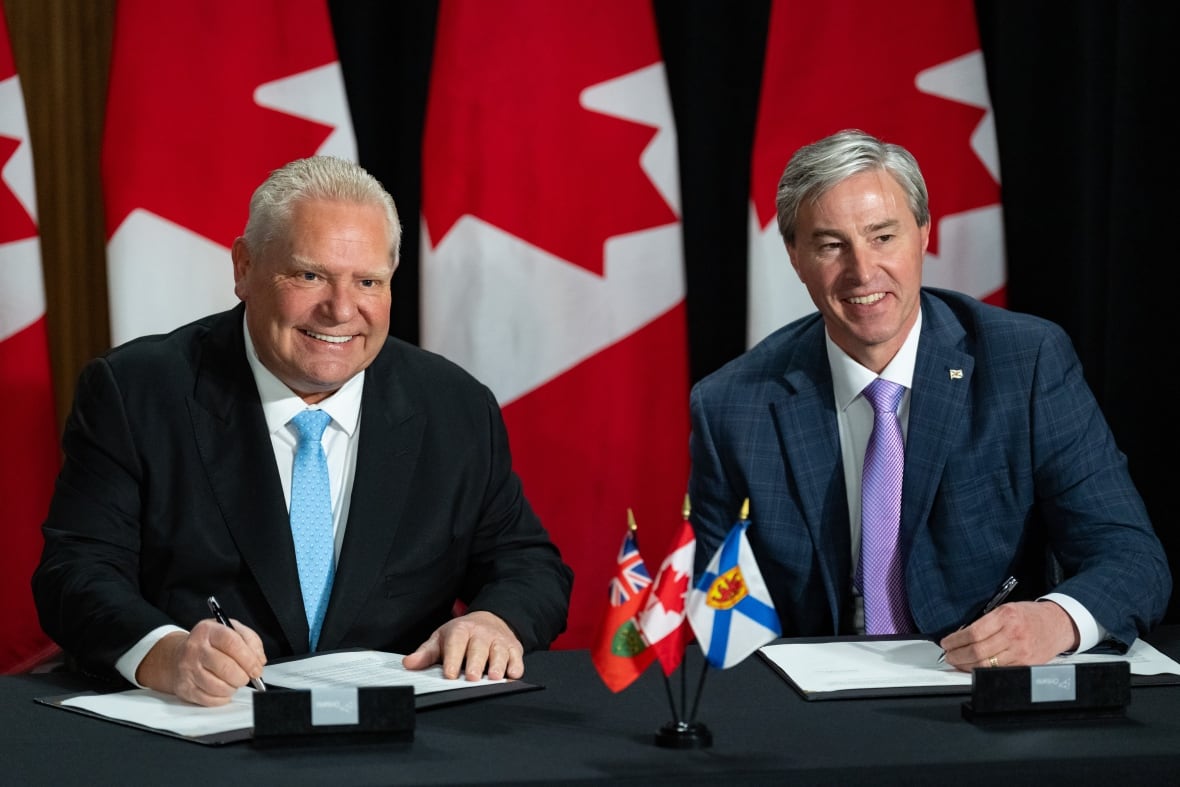 Two men smile while signing documents at a desk.
