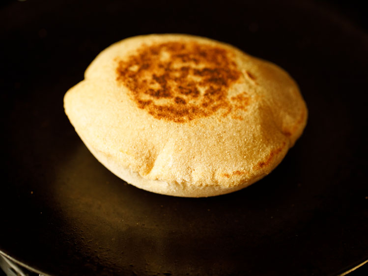 puffed up pita bread flipped over and the second side being roasted. 