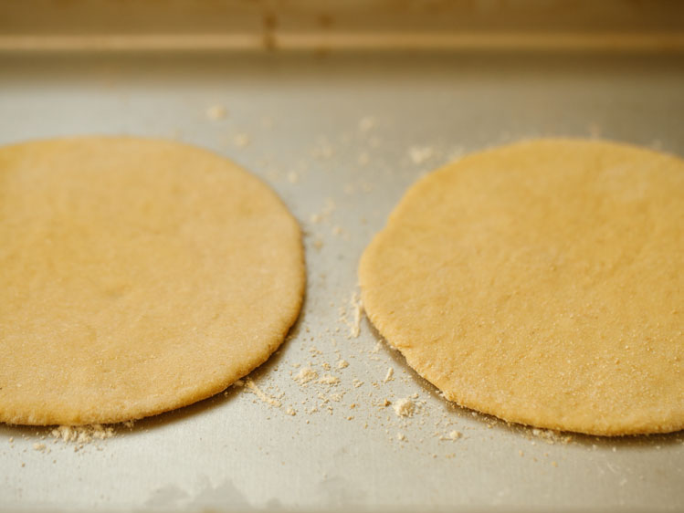 two rolled pita bread discs placed in the hot baking tray with some flour already sprinkled on the tray. 