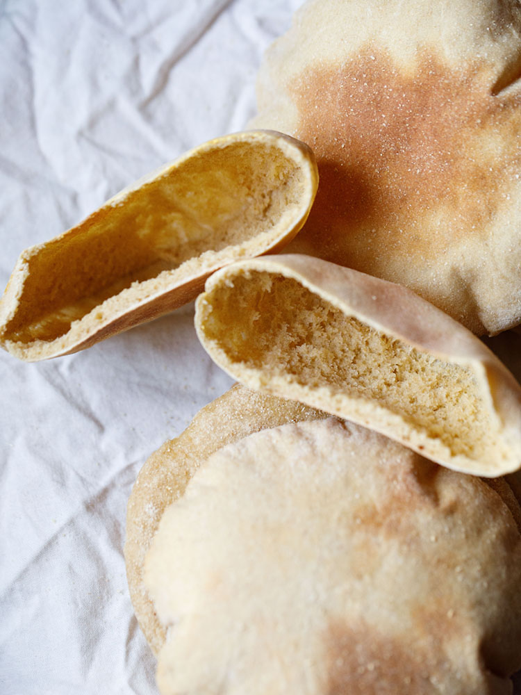 top view of pita bread pockets with three pita bread thrown around on a crumpled white cotton napkin. 