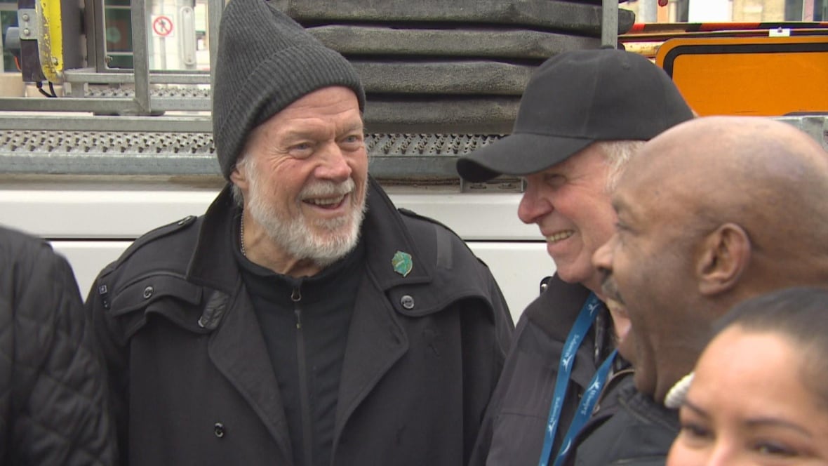 A man with a hat looks at others in the crowd smiling. 
