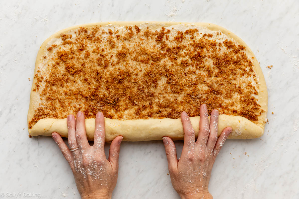 hands rolling up orange zest cinnamon roll filling.