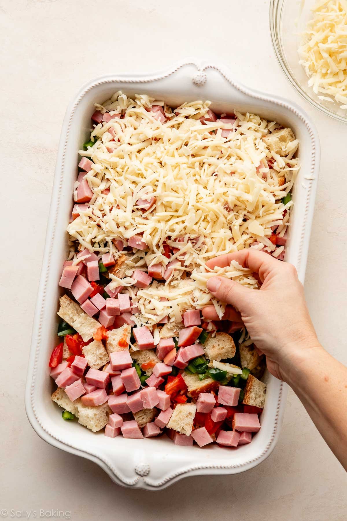 sprinkling cheese on cubed bread and ham.