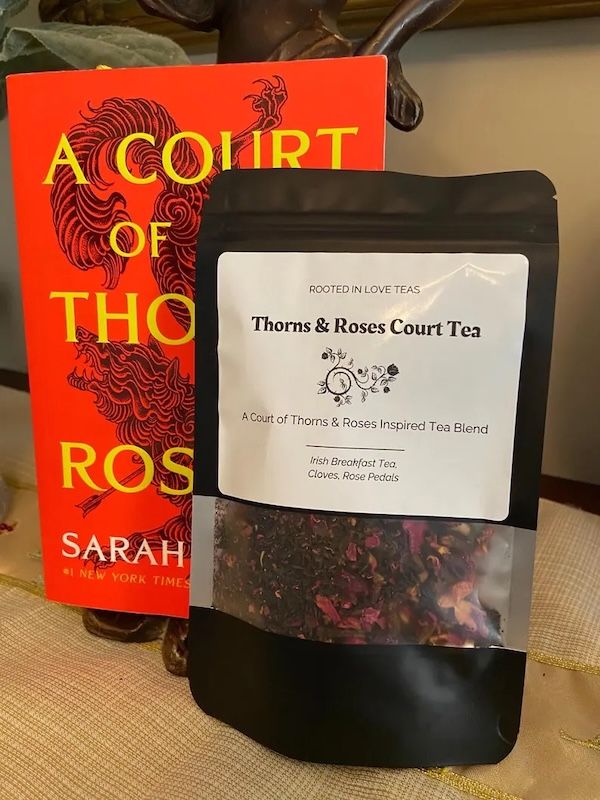 a black resealable pouch of loose lead tea with a a label for Thorns & Roses Court Tea next to a copy of A Court of Thorns and Roses by Sarah J Maas