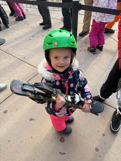 Young girl holding skis is about to ski with her grandparents. 