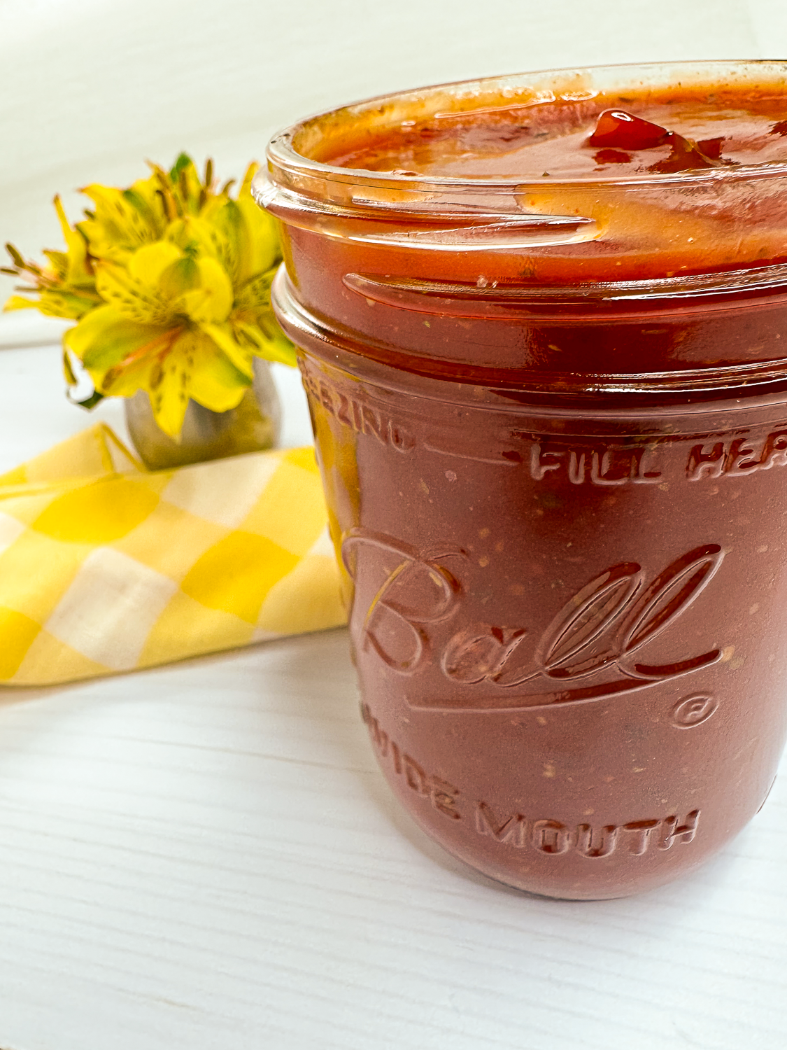 Cajun BBQ sauce in a clear Mason jar with yellow flowers and a yellow and white napkin.