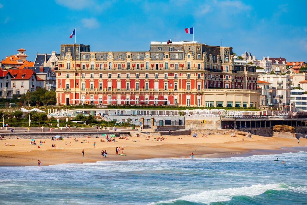 A grand hotel in orange and white, perched on a beach with big waves in Biarritz.