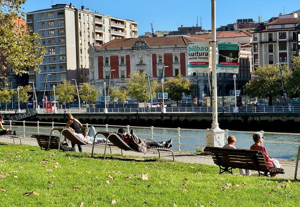 People sitting in lounge chairs along the edge of the river in Bilbao.