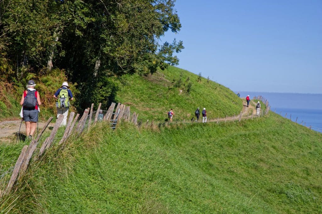 A line of hikers along a hiking path on a cliff along the sea.