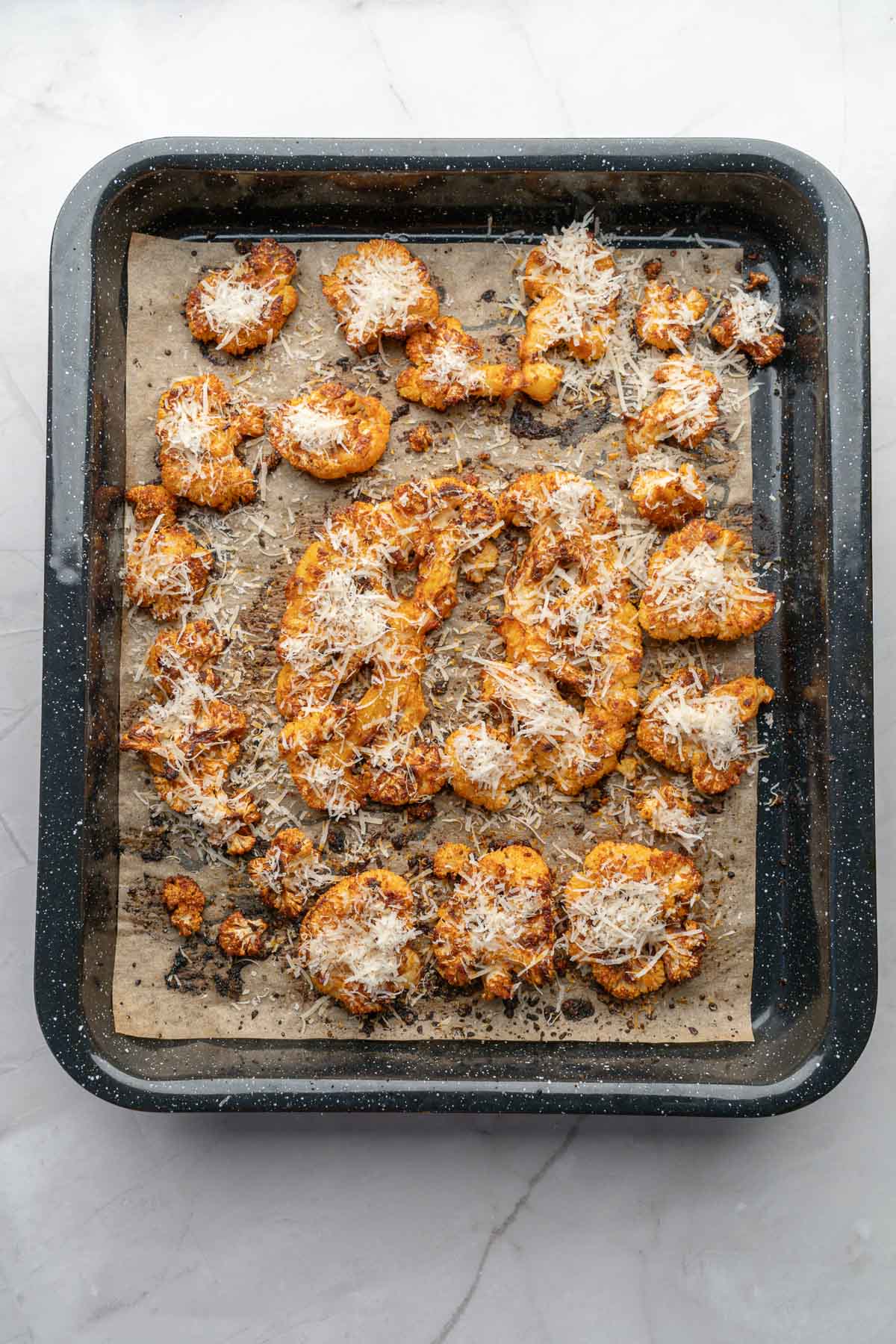 Roasted cauliflower steaks coated with grated cheese on a parchment-lined baking tray.