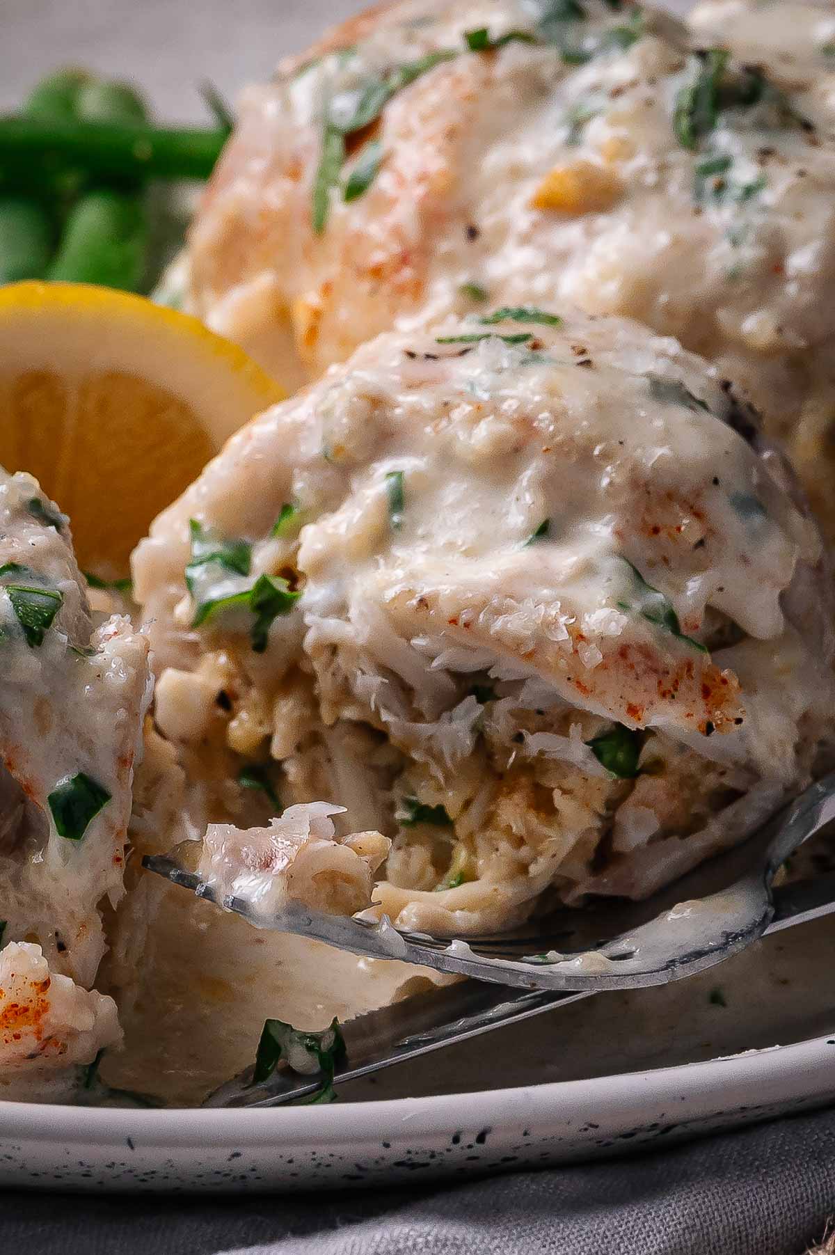 A close-up of a creamy baked crab stuffed flounder garnished with chopped herbs, served with a lemon wedge on a white plate.